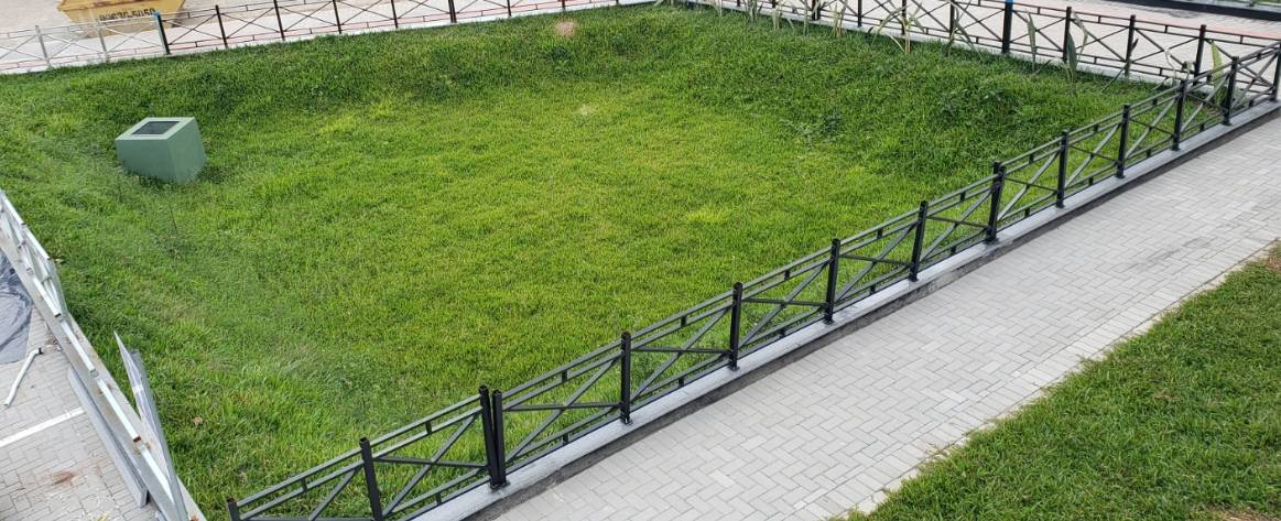 Espaço gramado cavado a um metro abaixo do nível da rua, gradeado e com uma tubulação de escape