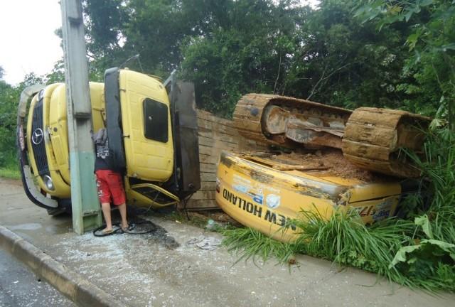 Caminhão transportando escavadeira fica sem freio, colide em poste e tomba