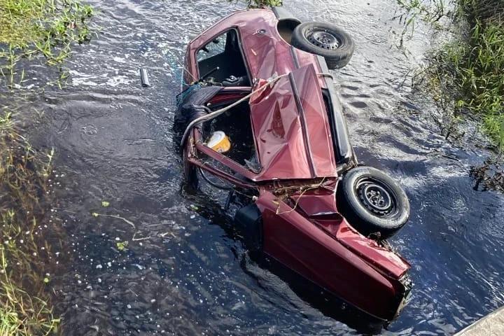 Carro sai da pista, capota e fica parcialmente submerso em riacho